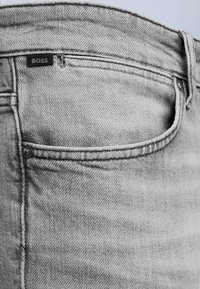 Jean en denim gris clair en gros plan montrant la poche avant, la passants de ceinture, les coutures cousues et une petite étiquette noire avec le texte « BOSS ».