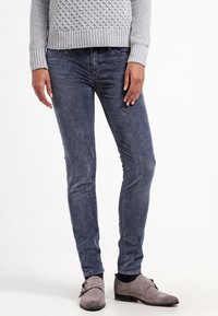 Smala, mörkblå jeans med en jämn yta, subtil blekning och femficksdesign, kombinerat med grå skor och en stickad grå tröja.