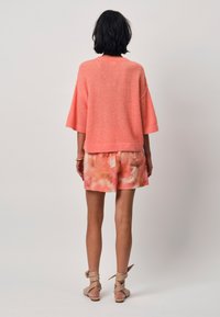 Korte mouw, koraalkleurige gebreide trui gecombineerd met pastel tie-dye shorts. De shorts hebben twee achterzakken en een relaxte pasvorm.