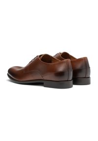 Zapatos de vestir de cuero marrón con un acabado suave, punta redonda, diseño de cordones y un tacón bajo y cuadrado. Acentos de costura sutiles.