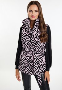 Zebra-mønstret vest i pink og sort, med høj krave, bælte i taljen og to forlommer, båret over en langærmet sort top.