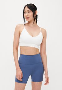 Soutien-gorge de sport blanc à côtes avec de fines bretelles et un design en V, associé à un short bleu ajusté taille haute en matière lisse.