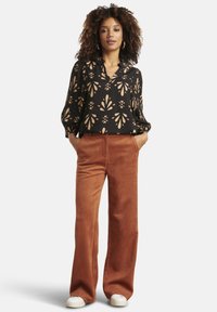 Black blouse with gold floral pattern, long sleeves, and a v-neck, paired with rust-colored wide-leg trousers and white sneakers.