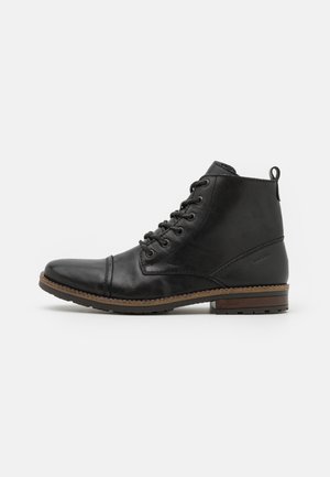 Botas de tobillo de cuero negro con punta redondeada, diseño de cordones y acabado texturizado. Presentan un pequeño tacón y costuras reforzadas.