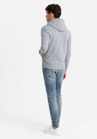 Sweat à capuche gris avec cordon de serrage, tissu texturé et poignets côtelés. Assorti avec un jean bleu clair et des baskets blanches. Vue de dos.