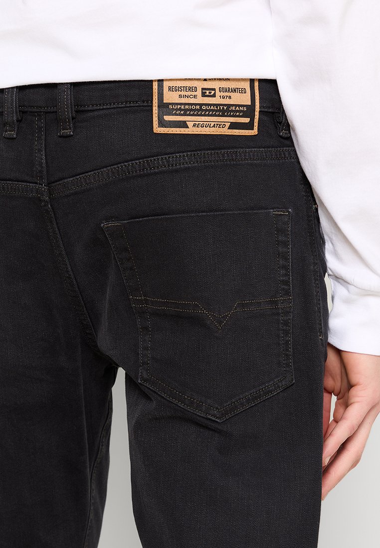 Jean en denim noir avec une poche arrière à rabat pointu, des détails de couture subtils et un patch en cuir de la marque au niveau de la taille.