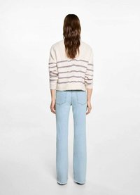 Suéter de punto crema con rayas horizontales moradas, diseño recortado. Combinado con jeans acampanados de color azul claro con dobladillos sin rematar.