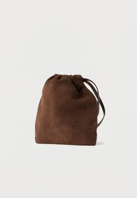 Brązowa zamszowa torba na sznurek o miękkiej fakturze, zaokrąglonym kształcie i cienkim pasku. Na przedniej stronie znajduje się subtelne wytłoczone logo.