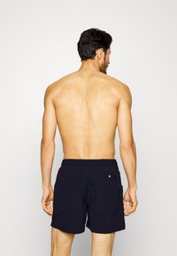 Shorts da nuoto blu navy in materiale leggero con vita elastica, dotati di una tasca posteriore e dettagli in rosso, bianco e blu.