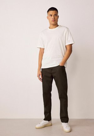 Weißes Kurzarm-T-Shirt, dunkelgrüne Hose und weiße Sneaker. Einfaches Design, lockere Passform. Glatte Textur, keine sichtbaren Muster oder Akzente.