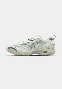 Zapatilla atlética blanca de malla con acentos verdes, superposiciones texturizadas, cordones y una pestaña de agarre; cuenta con una suela gruesa con patrones de tracción.