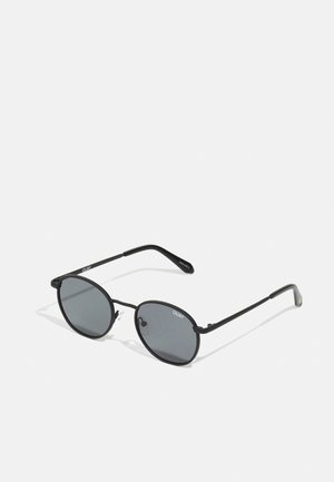 Ochelari de soare ovali negri cu lentile închise, cadru subțire din metal negru și pernuțe nazale transparente. Brațele au logo-ul brandului. Design minimalist.