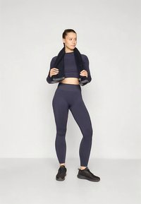 Mörkblå atletiskt set som inkluderar en figurnära långärmad topp och högmidjade leggings. Materialet är mjukt med en stretchig känsla. Svarta sneakers används.