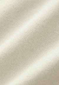 Pleteni materijal u nježnoj krem bojii, s glatkom, teksturiranom površinom koja ima konzistentan uzorak šavova i suptilne varijacije.