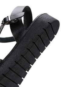 Sandale noire à semelle plate avec un motif strié. Fabriquée en cuir textur�é, elle possède une sangle réglable avec une boucle en métal.