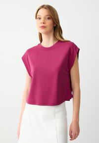 T-shirt fucsia cropped con maniche corte, scollatura rotonda e spacchi laterali; tessuto in morbido misto cotone con una texture leggera.