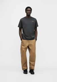 Γκρι βαμβακερό κοντομάνικο μπλουζάκι με μικρό χρυσό λογότυπο, συνδυασμένο με ταμπά παντελόνι cargo και μαύρα αθλητικά παπούτσια. Απλός, άνετος σχεδιασμός.