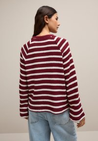 Maglione a righe bordeaux e bianche con maniche lunghe e collo stondato, realizzato in materiale morbido e testurizzato. Presenta una vestibilità rilassata e polsini a coste.