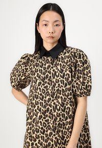 Rochie cu imprimeu leopard, având o bază bej, guler negru și mâneci bufante cu manșete elastice. Țesătură netedă cu modele variate pe întreaga suprafață.