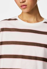 Puuvillane t-särk, millel on horisontaalsed triibud pruunis, heleroosas ja valges. Ümara kaelusega ja pehme tekstuuriga, rõhutades juhuslikku disaini.