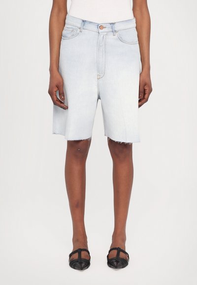 Shorts de mezclilla de color azul claro con un dobladillo deshilachado, cinco bolsillos y cierre de botón. Combinados con unas sandalias planas negras con tiras.