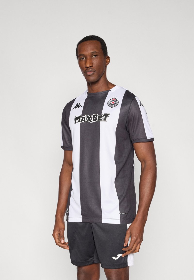 Sort og hvidt sportsjersey med korte ærmer, med rund halsudskæring og logoer. Bæres med sorte shorts for et koordineret udseende.