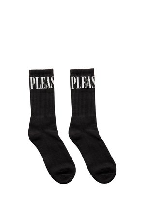 Para czarnych skarpet sportowych z białym napisem "PLEASE" blisko górnego ściągacza, ułożonych płasko na białym tle.