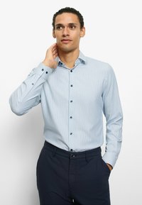 Light blue button-up shirt with fine stripes, contrasting dark buttons, and long sleeves. Paired with dark trousers. Classic collar design.