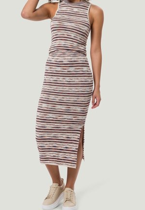 Femme portant une robe midi sans manches, à col haut, à rayures multicolores horizontales avec une fente latérale, associée à des baskets compensées beiges.