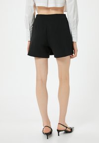 Pantaloni corti neri su misura con vita media, tessuto morbido e taglio classico. Indossati con una camicia bianca corta e sandali neri con tacco.
