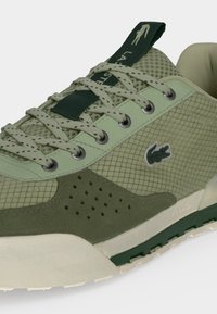 Ανοιχτό πράσινο παπούτσι Lacoste με πάνελ από δίχτυ και σουέντ, διάτρητες λεπτομέρειες, κορδόνια με σχέδιο και λογότυπο στο πλάι και στη γλώσσα.