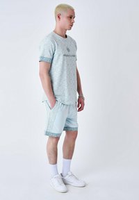 Ensemble de sport bleu clair comprenant un t-shirt à manches courtes à motifs et un short assorti, tous deux ornés de motifs géométriques et d'accents de logo.