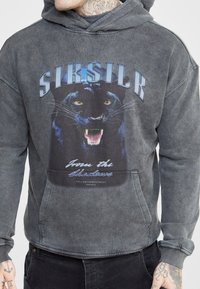 Felpa grigia scura con una grafica di pantera sulla parte anteriore, con il testo "SIKSILK" e "Dall'ombra." Tessuto morbido con una vestibilità rilassata.