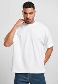 T-shirt bianco in cotone con vestibilità ampia e collo a giro. Presenta maniche corte e una trama liscia. Abbinato a jeans in denim blu.