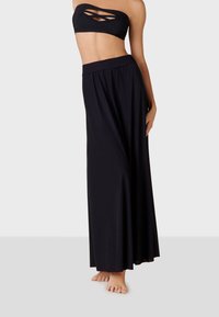 Svart bandeau-bikinitopp med utskärningar som matchas med en lång svart maxikjol, slät textur, elastisk midja och flödande design.