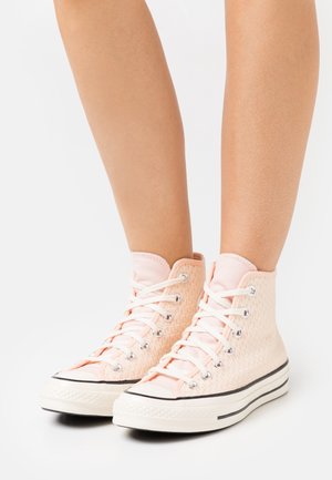 Höga sneakers i mjuk persikofärgad tyg med texturerade överlägg, vita gummi-sulor och klassiska svarta detaljer. Har metallögon och snören.