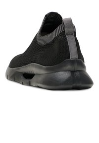 Black athletic shoe featuring a breathable mesh upper, elastic collar, and a textured rubber sole with a cutout for flexibility.