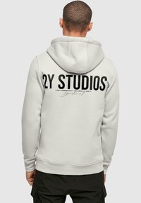 Hoodie grigio chiaro con una grande stampa nera "2Y STUDIOS" sul retro. Presenta un cappuccio con cordino e polsini e orlo a coste.