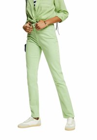 Jeans en coton vert clair avec une coupe slim, dotés d'une fermeture à boutons et zip, de poches latérales, et assortis à des baskets blanches.