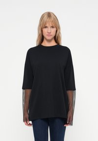 Μαύρο oversized t-shirt με μακριά μανίκια από δίχτυ. Από μαλακό βαμβακερό ύφασμα, στρογγυλή λαιμόκοψη, χαλαρή εφαρμογή και υφασμάτινες λεπτομέρειες στα μανίκια.