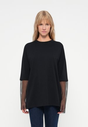 Schwarzes oversized T-Shirt mit langen Mesh-Ärmeln. Weiches Baumwollmaterial, runder Ausschnitt, lockere Passform und strukturierte Akzente an den Ärmeln.