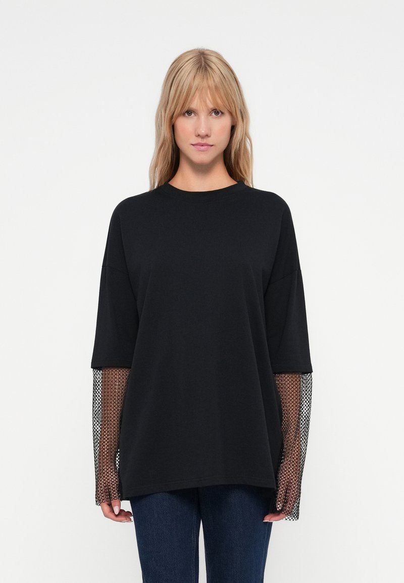 Μαύρο oversized t-shirt με μακριά μανίκια από δίχτυ. Από μαλακό βαμβακερό ύφασμα, στρογγυλή λαιμόκοψη, χαλαρή εφαρμογή και υφασμάτινες λεπτομέρειες στα μανίκια.