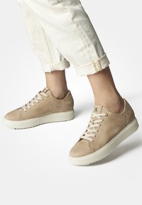 Baskets en cuir beige avec une finition lisse, un bout arrondi et une semelle en caoutchouc de couleur claire. Présente des lacets ton sur ton et de légères perforations décoratives.