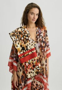 Sciarpa in misto seta con stampa leopardata, caratterizzata da strisce rosse e un logo a contrasto. Tessuto trasparente con bordi asimmetrici.