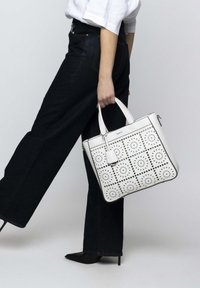 Weiße Leder-Tote-Bag mit durchbrochenen KreisMustern, quadratischem Design, silbernen Beschlägen, doppelten Griffen und einem abnehmbaren Tag.