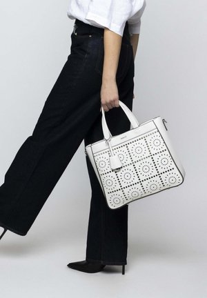 White leather tote bag with perforated circular patterns, square design, silver hardware, dual handles, and a removable tag.