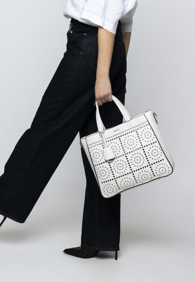 Weiße Leder-Tote-Bag mit durchbrochenen KreisMustern, quadratischem Design, silbernen Beschlägen, doppelten Griffen und einem abnehmbaren Tag.