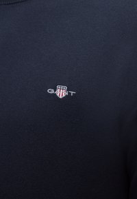 Tissu tricot bleu foncé avec petit logo GANT brodé présentant un écusson avec des étoiles et des rayures en blanc et rouge.
