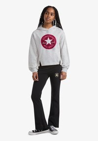 Siva cropped jopa s kapuco in rdečim krogličnim logotipom, kombinirana s črnimi razširjenimi trenirkami z zlatim logotipom. Črne superge zaključujejo izgled.