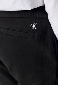 Černé bavlněné tepláky s žebrovaným pasem, malým bílým logem "ck" a zadní kapsou s diskrétními švy.